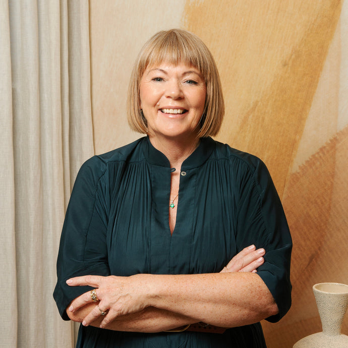 Woman in a dark blue dress standing in front of a textured wall with a vase on a table.